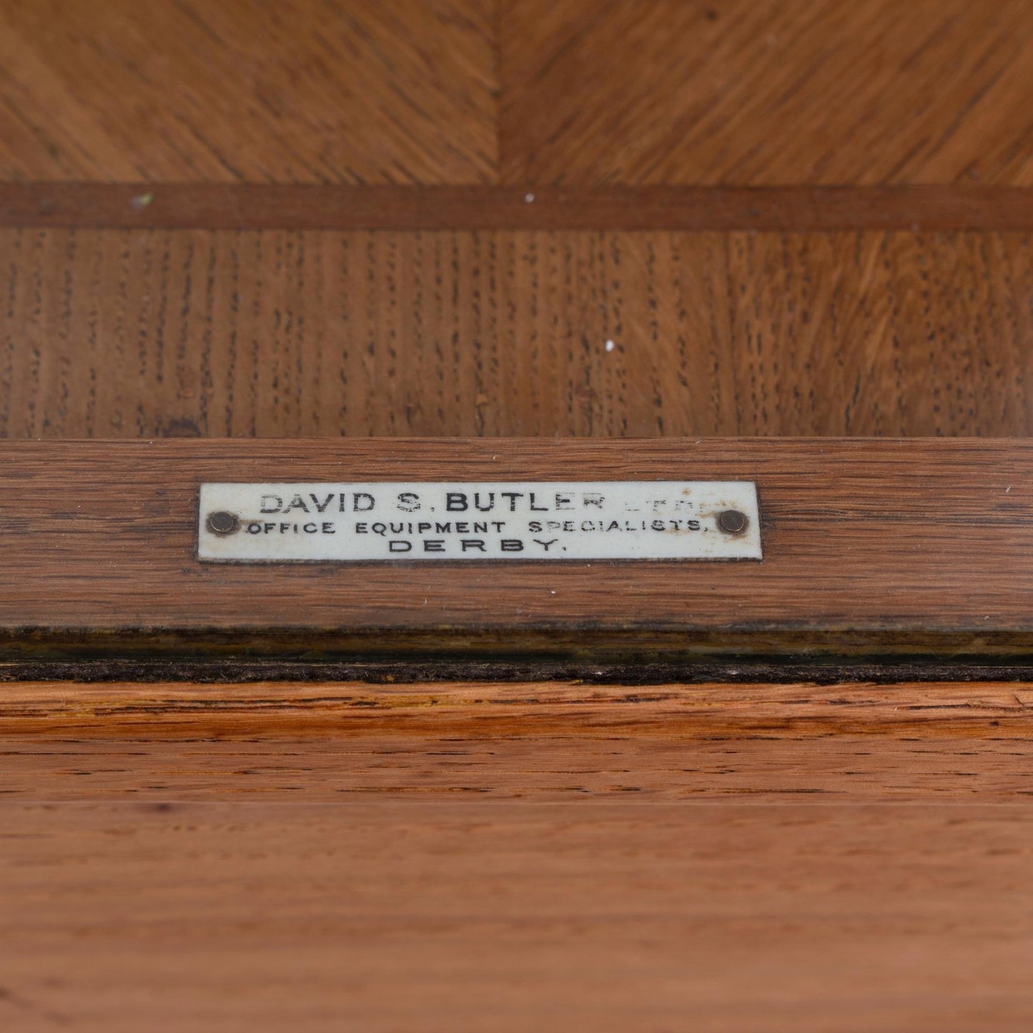 Dettaglio targhetta Bancone vetrina inglese in legno di rovere, risalente alla prima meta del '900, con due mensole e ante scorrevoli in vetro.  Riporta la targhetta originale "David S. Butler ltd office equipment specialists Derby".