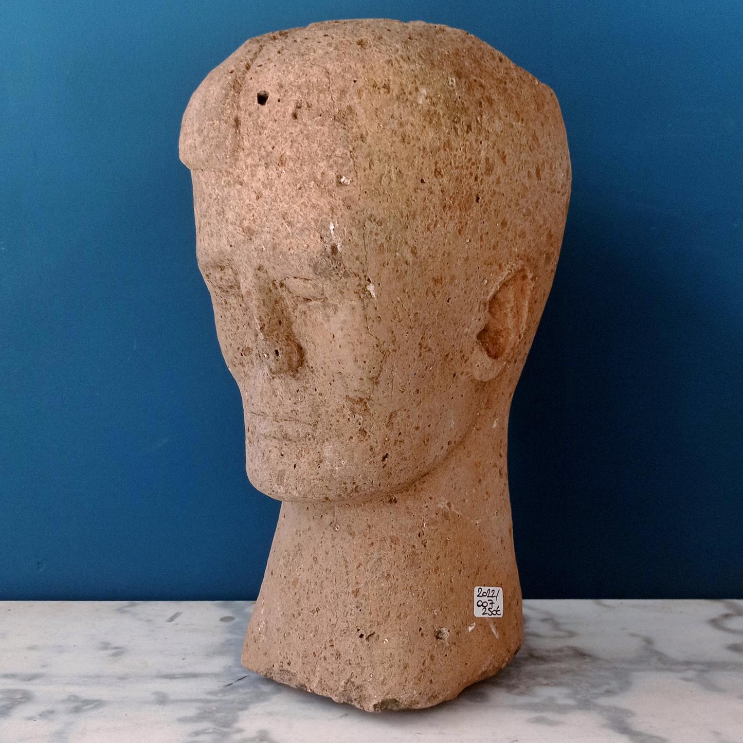 Scultura in peperino rosa raffigurante una testa di ispirazione etrusca, prodotta in Italia nella prima metà del '900.